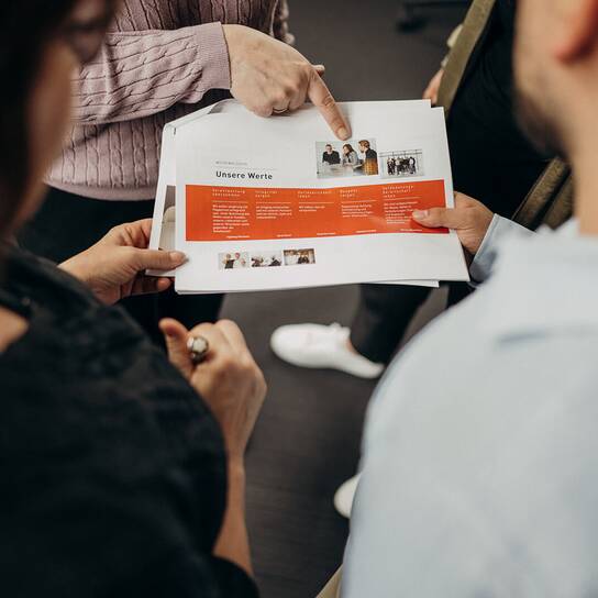 A group of people discusses a document featuring company values during a collaborative meeting.