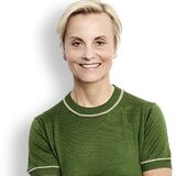A smiling woman in a green top stands confidently against a white background.