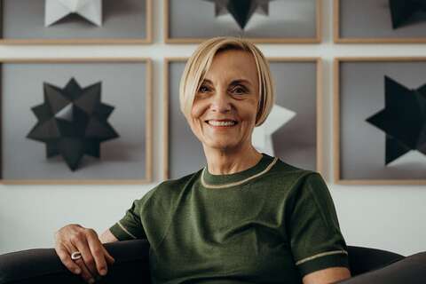 A person in a green shirt sits on a chair, smiling, with geometric star art on the wall behind them.